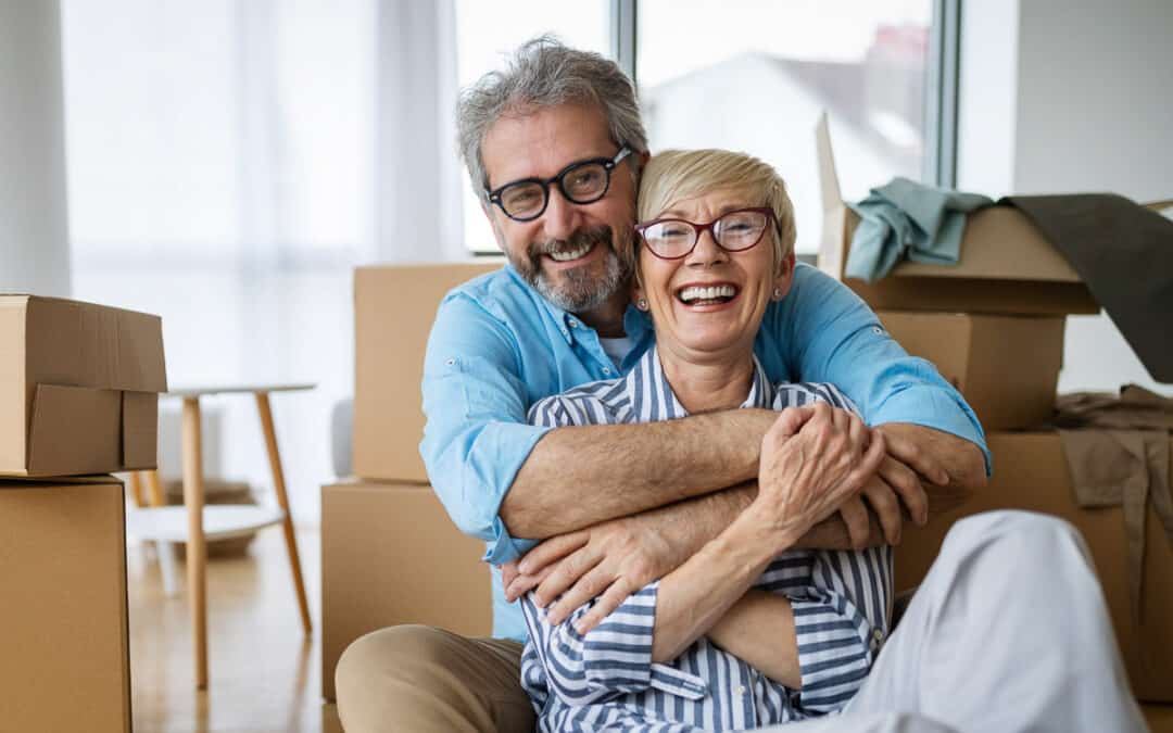 Senior couple embracing joyfully in a living room filled with moving boxes, celebrating a new home.