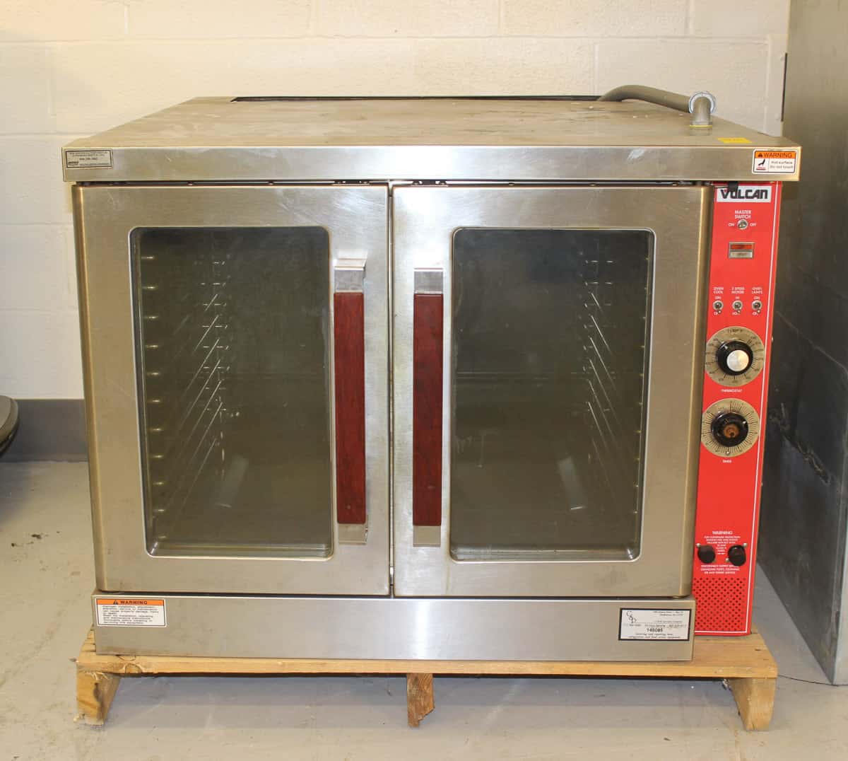 A commercial Vulcan convection oven with double glass doors and red control knobs, placed on a wooden stand.
