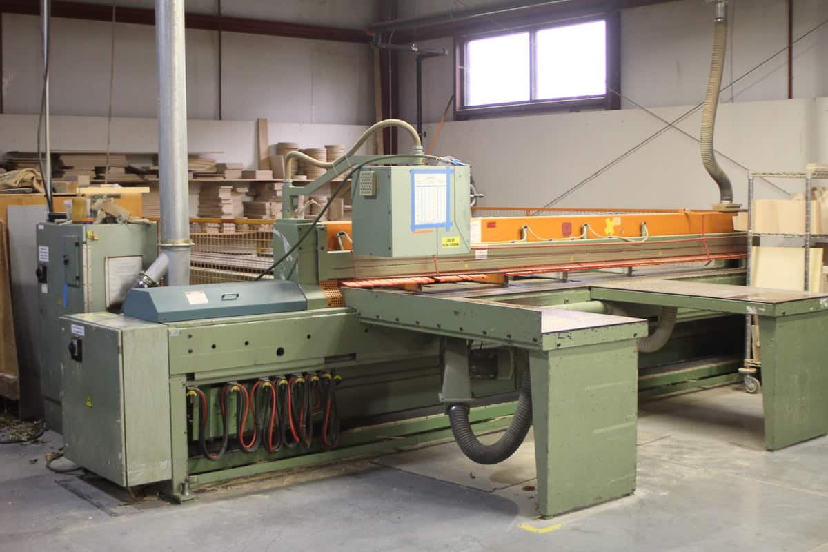 Industrial woodworking machinery in factory with large conveyor machine and stacked wood in the background.