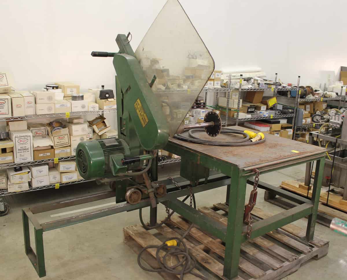 Industrial metal cutting saw in a workshop with scattered boxes and tools.