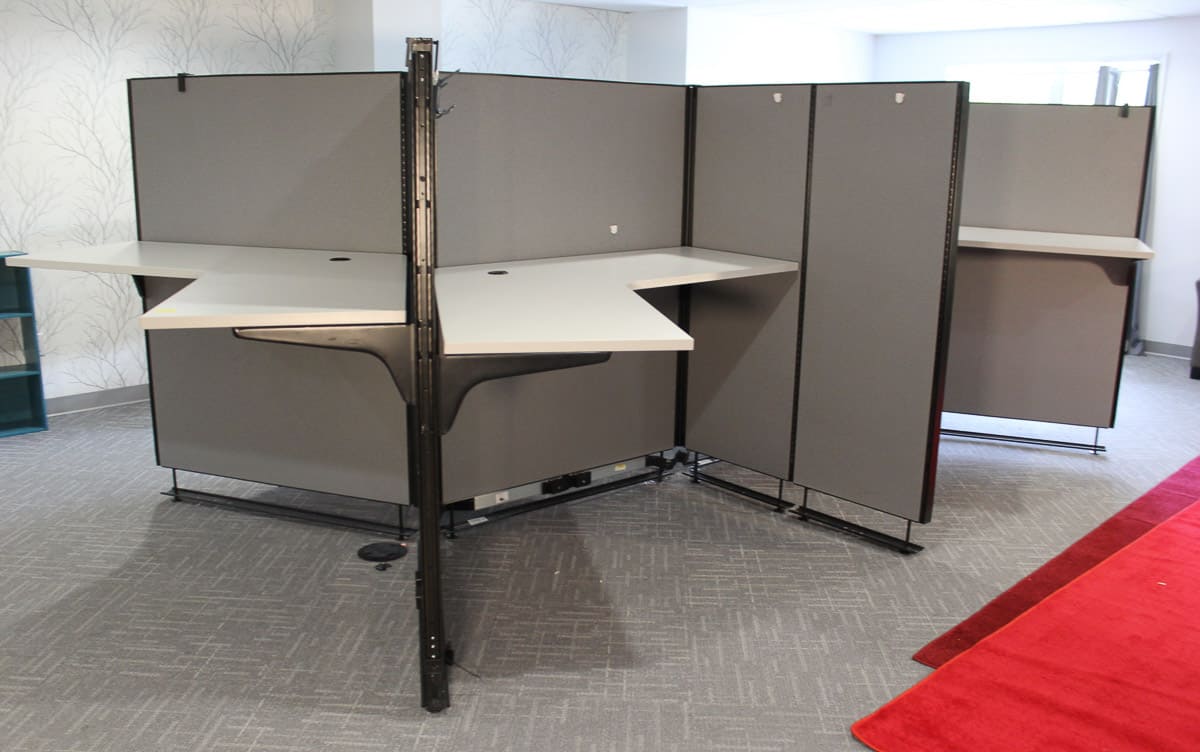 An empty modern office cubicle setup with multiple partitions and standing desks on a patterned carpet.