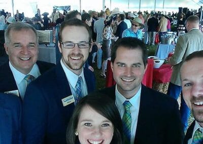 Four men and one woman, all dressed in business attire. smiling at a fundraiser under a white tent.