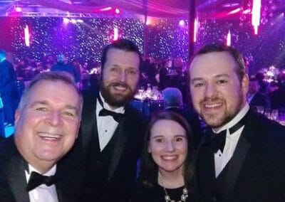 Four people smiling at a gala event, dressed in formal attire, with a glittering lights background.