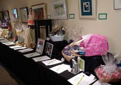 A charity auction event showcasing various gift baskets and framed artworks displayed on or by a table.