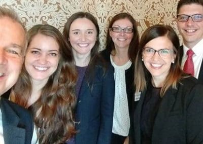 Six professionals smiling for a group photo, with a decorative wallpaper background.