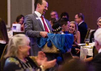 A man holding a basket smiles while interacting with guests at a fundraising event.