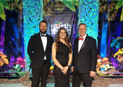 Three people in formal attire at an event with a tropical-themed backdrop featuring the logo "North Fulton Community Charities.