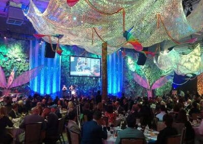 A room decorated with glittering fabrics and colorful lights, filled with guests seated at tables during an event.