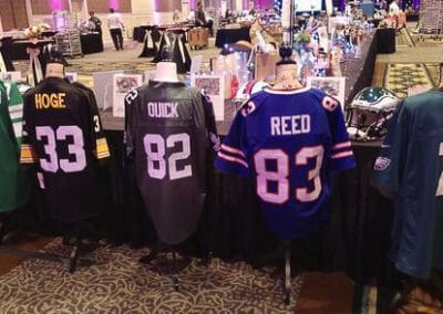 Assorted sports jerseys displayed on mannequins at a charity auction event in a large, carpeted banquet hall.