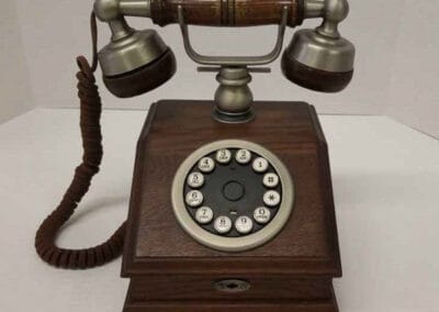 Vintage wooden rotary dial telephone with a classic handset and curly cord on a white background.