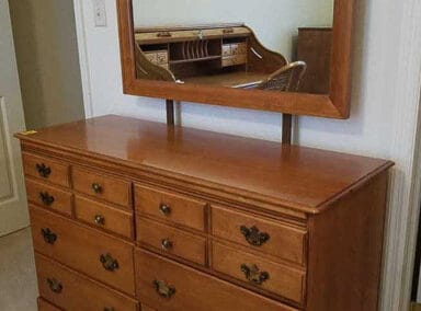 A wooden dresser with multiple drawers and a square mirror reflecting a room interior.