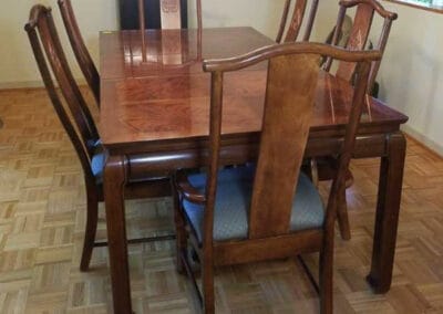 A polished wooden dining table with six matching chairs set on a parquet floor in a room with beige walls.