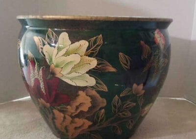 Green ceramic bowl with a floral design up for auction, placed on a carpeted surface.