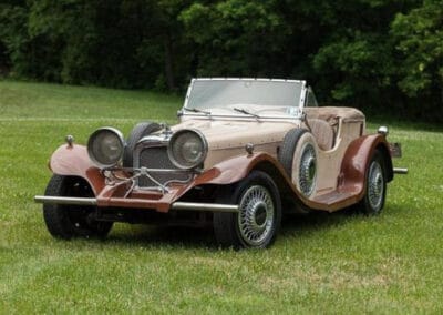 A vintage convertible car with large headlights parked on a grass field.