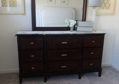 A wooden dresser with a large mirror, flanked by two pieces of framed artwork, in a room with beige carpeting.