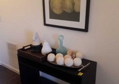 A hallway featuring a black console table with decorative balls, a turquoise vase, and a framed picture of pears hanging above.