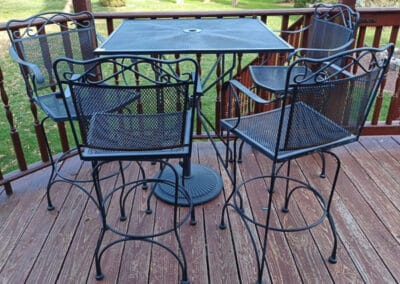 A patio set featuring a round metal table and four chairs with intricate designs, on a wooden deck.