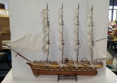A detailed scale model of a sailing ship with multiple masts and sails, displayed on a stand against a white backdrop.
