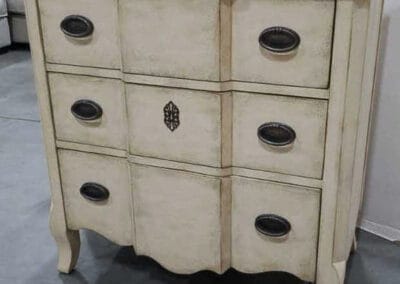 Vintage cream-colored dresser with nine drawers, round metal handles, and a decorative emblem in the center.