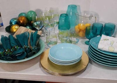 Vintage table set with turquoise and gold tableware, including plates, glasses, and decorative items on a white surface.
