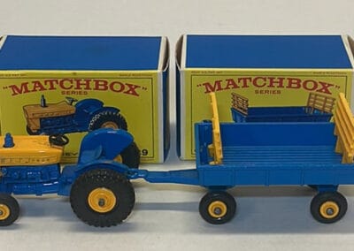 Vintage Matchbox tractor toy in yellow and blue, connected to a blue detachable trailer, displayed in front of their original boxes.
