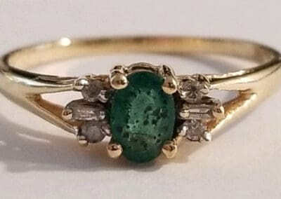 Gold ring featuring an oval emerald flanked by small diamonds set on a white background.