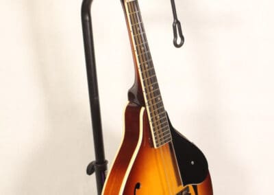 A mandolin with a sunburst finish resting on a black metal stand against a plain, light background.