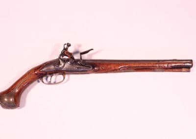 Antique flintlock pistol with intricate metalwork and wooden grip on a light pink background.