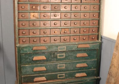 An old, tall wooden cabinet with multiple rows of small drawers and larger drawers at the bottom, painted partially in green.