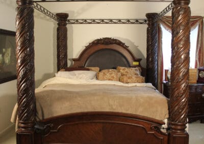 An ornate wooden four-poster bed with carved posts and a canopy frame, set in a bedroom with traditional decor.
