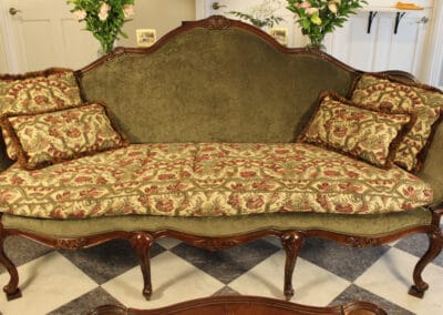 An antique couch with floral-patterned cushions, ornate wooden frame, and green upholstery in a room with a checkered floor.