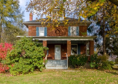 A quaint two story brick house surrounded by green foliage and bright autumn leaves, under a clear sky.