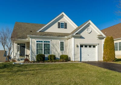 A suburban house with white siding, a single-car garage, gabled roof, and a well-maintained lawn under a clear blue sky.