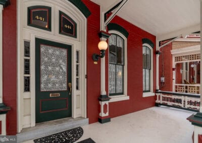 An elegant covered porch featuring red walls, a green door with ornate glasswork, and white trim around arched windows.