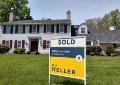 "Sold" sign from H. K. Keller in front of a two-story house with red shutters and white siding under a clear blue sky.