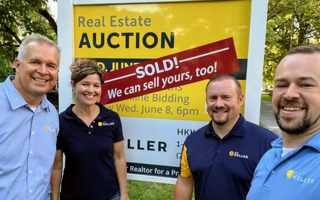 Four people smiling in front of a real estate auction sign that announces a property sold.