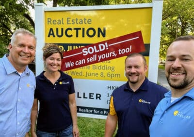 Four people smiling in front of a real estate auction sign that announces a property sold.