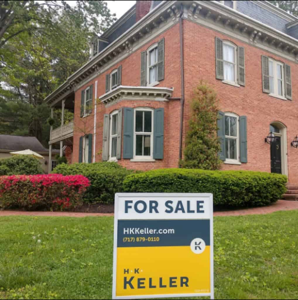 A two-story brick house with white trim and a "for sale" sign from H. K.. Keller in the front yard.