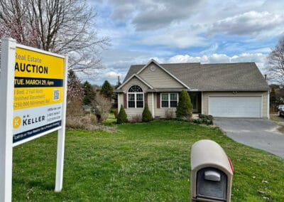 A single-story suburban home with a "real estate auction" sign posted in the front yard under a cloudy sky.