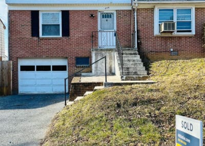 Two-story duplex house with a white and brick exterior and a "sold" sign in the front yard.