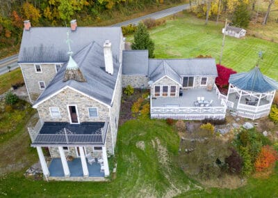 Aerial view of a stone house with an adjacent gazebo, surrounded by trees displaying autumn foliage.